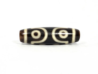 Third lateral profile of antique Tibetan seven-eye dzi bead showing two large eyes with scroll connectors and cream-white rings on deep brown-black agate ground, 39.7 mm × 11.7 mm