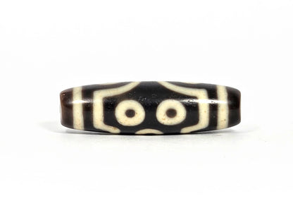 Fourth lateral profile of antique seven-eye dzi bead (AT-092826-7E) showing two eyes in paired arrangement with angular bracket framing elements, dark brown-black and cream-white agate