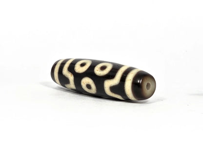 Angled end view of antique Tibetan seven-eye dzi bead showing small clean drill hole set in warm brown agate end cap, elongated barrel form, 200–400 years old
