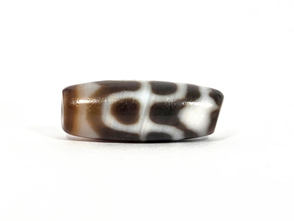 Third lateral profile of vintage Taiwan chalcedony dzi bead N-B-101426-TTL showing full barrel — cream-white tiger tooth and lotus motif with high-gloss chalcedony polish visible, dark warm brown ground, squat barrel form