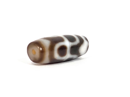 Opposite angled end view of vintage Taiwan chalcedony dzi bead N-B-101426-TTL showing second drill hole at warm amber-brown chalcedony tip with bloodspot patina visible, tiger tooth and lotus motif along barrel