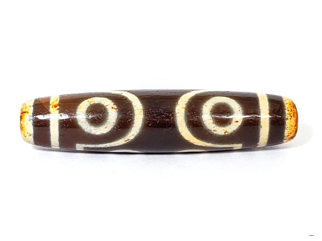 A vintage Dzi bead with a faux antique appearance featuring a captivating seven-eye motif. The bead showcases intricate carvings, with seven eyes symbolizing protection, intuition, and spiritual awakening