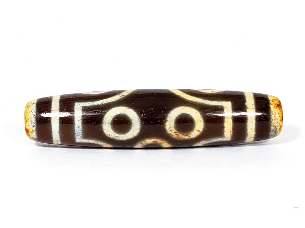 A vintage Dzi bead with a faux antique appearance featuring a captivating seven-eye motif. The bead showcases intricate carvings, with seven eyes symbolizing protection, intuition, and spiritual awakening