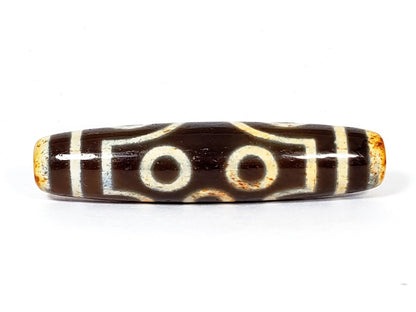 A vintage Dzi bead with a faux antique appearance featuring a captivating seven-eye motif. The bead showcases intricate carvings, with seven eyes symbolizing protection, intuition, and spiritual awakening
