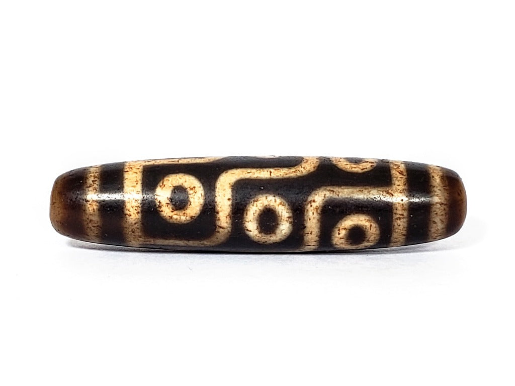 A vintage Dzi bead with a faux antique appearance featuring a captivating nine-eye motif. The intricate patterns and worn texture give it an ancient and mystical allure.