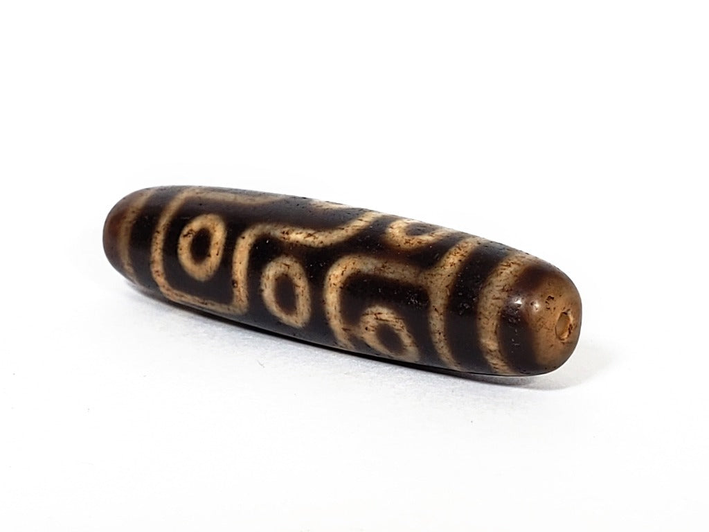 A vintage Dzi bead with a faux antique appearance featuring a captivating nine-eye motif. The intricate patterns and worn texture give it an ancient and mystical allure.