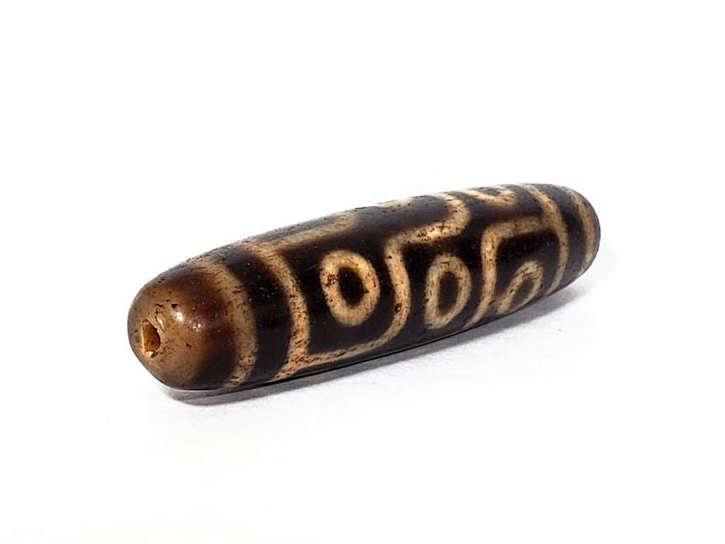 A vintage Dzi bead with a faux antique appearance featuring a captivating nine-eye motif. The intricate patterns and worn texture give it an ancient and mystical allure.