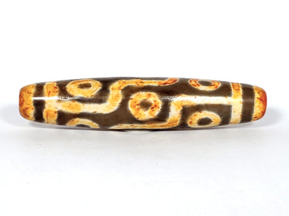A vintage Dzi bead with a faux antique appearance featuring a mesmerizing nine-eye motif. The bead showcases intricate carvings, with nine eyes symbolizing protection, insight, and spiritual power. 