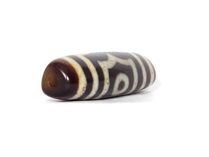 A vintage Dzi bead featuring a rare triangular shape and a captivating Three Eye Motif. This authentic artifact showcases the unique design and spiritual symbolism of ancient Dzi beads