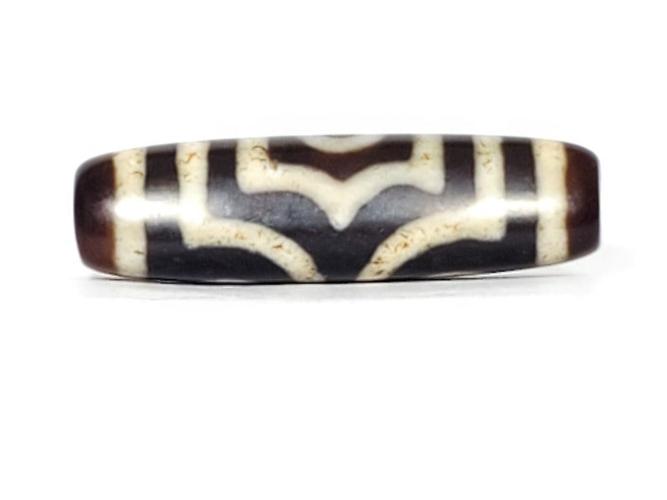 A vintage Dzi bead featuring a rare triangular shape and a captivating Three Eye Motif. This authentic artifact showcases the unique design and spiritual symbolism of ancient Dzi beads