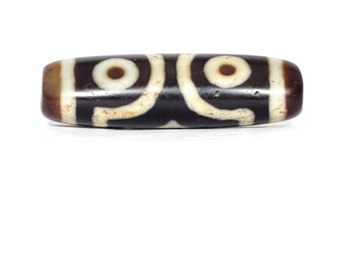 A vintage Dzi bead featuring a rare triangular shape and a captivating Three Eye Motif. This authentic artifact showcases the unique design and spiritual symbolism of ancient Dzi beads