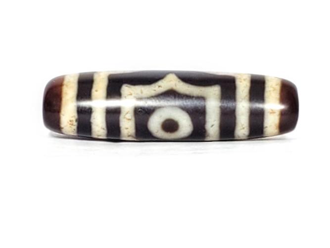 A vintage Dzi bead featuring a rare triangular shape and a captivating Three Eye Motif. This authentic artifact showcases the unique design and spiritual symbolism of ancient Dzi beads